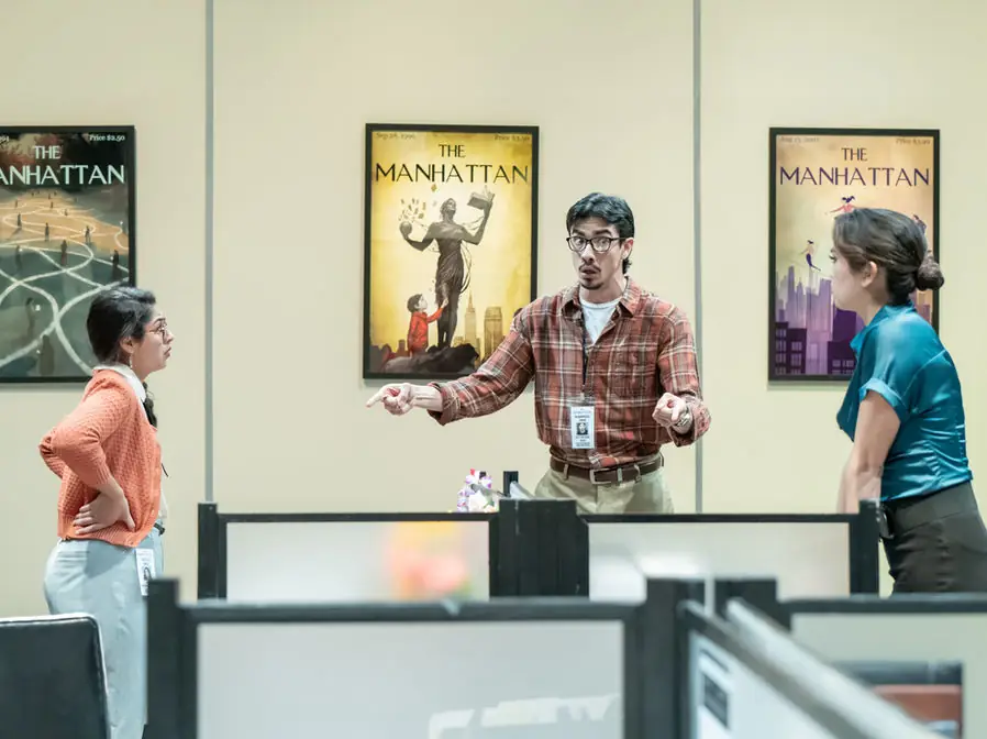 Production photo from Gloria showing performers in Gretchen Ugalde's sleek alley-stage office environment at UCI.